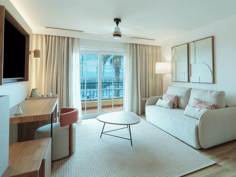 Bright living room with sofa, coffee table, desk, and balcony view of the sea.