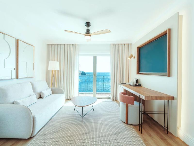 Bright living room with sofa, table, desk, and balcony overlooking the sea