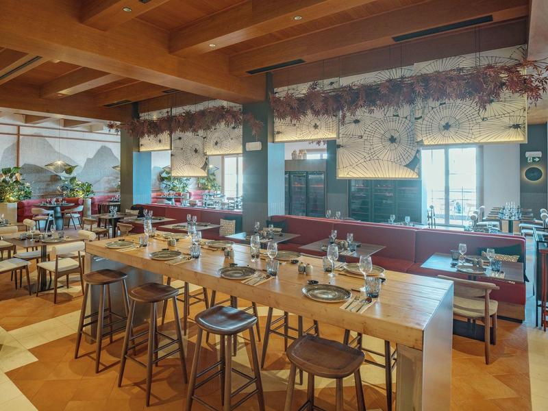 Cozy restaurant with wooden tables and chairs, red upholstered seating, and floral arrangements.