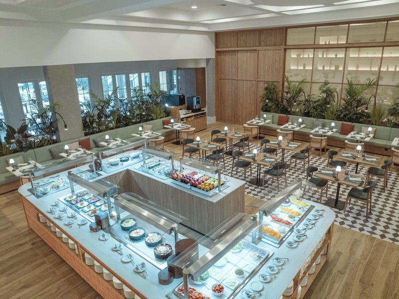 Modern hotel restaurant with buffet, stylish seating, and decorative plants.