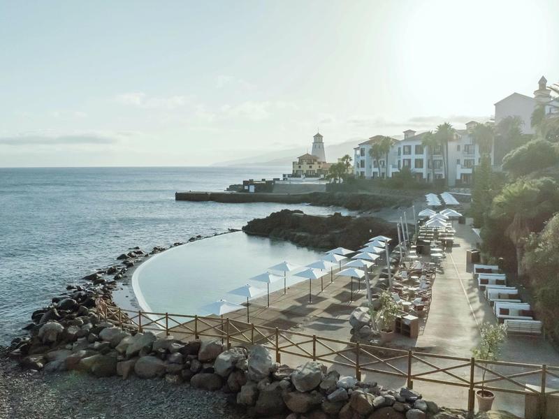 Small private beach with sun umbrellas and a view of the sea and adjacent buildings.
