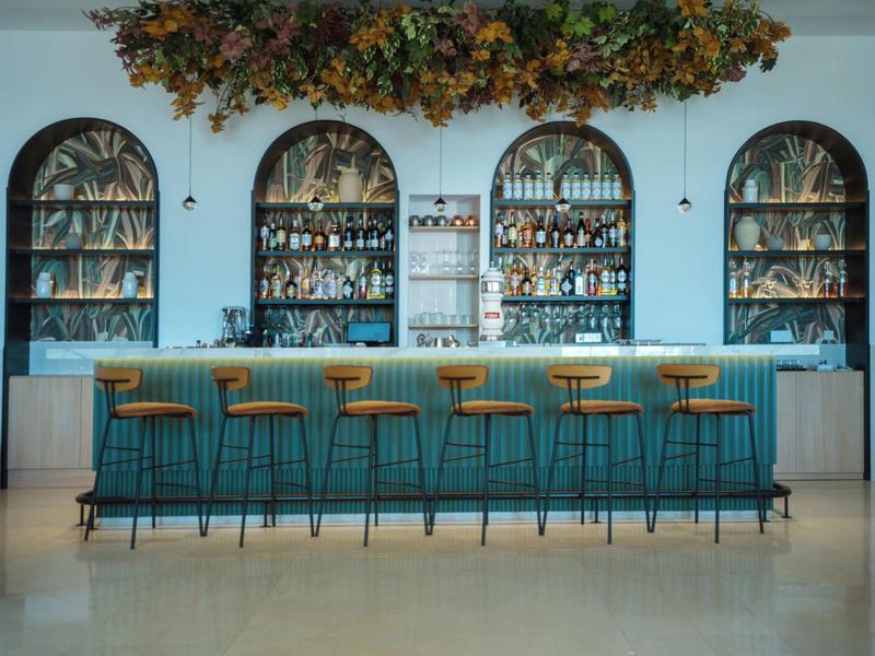 Modern hotel bar area with blue curtains, bar stools, and decorative plants.