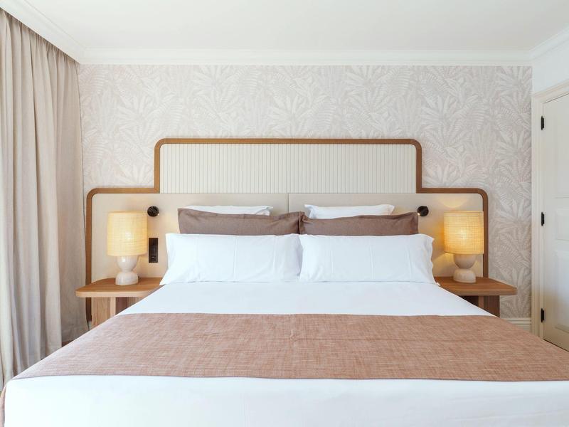 Modern hotel room with large double bed, two bedside tables, and warm lighting.