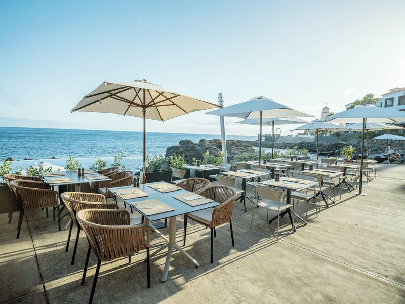 Outdoor restaurant with tables, chairs, and umbrellas by the sea