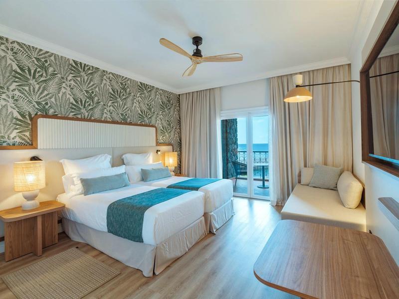 Modern hotel room with double bed, seating area, and balcony view.