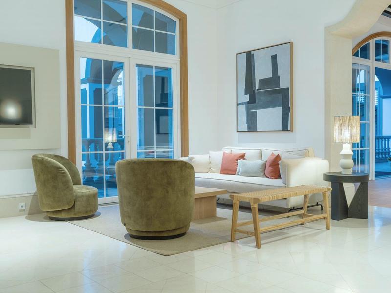 Bright living space with tall windows, comfortable armchairs, and sofa next to coffee table.