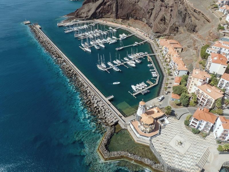Harbor with many sailboats, surrounded by rocks and buildings by the water.