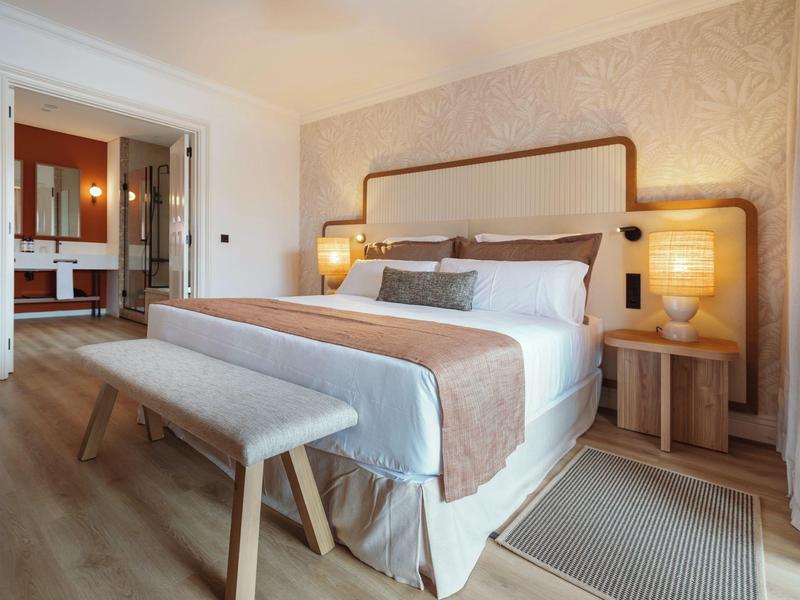 Modern hotel room with double bed, bench, and open bathroom area.