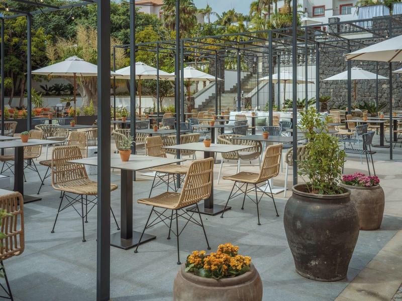 Empty outdoor hotel area with tables, chairs, and umbrellas on a terrace.