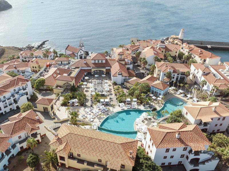 Aerial view of a Mediterranean hotel with pool, sun umbrellas, and sea view.