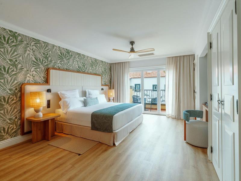 Brightly furnished hotel room with double bed, balcony, and modern decor.