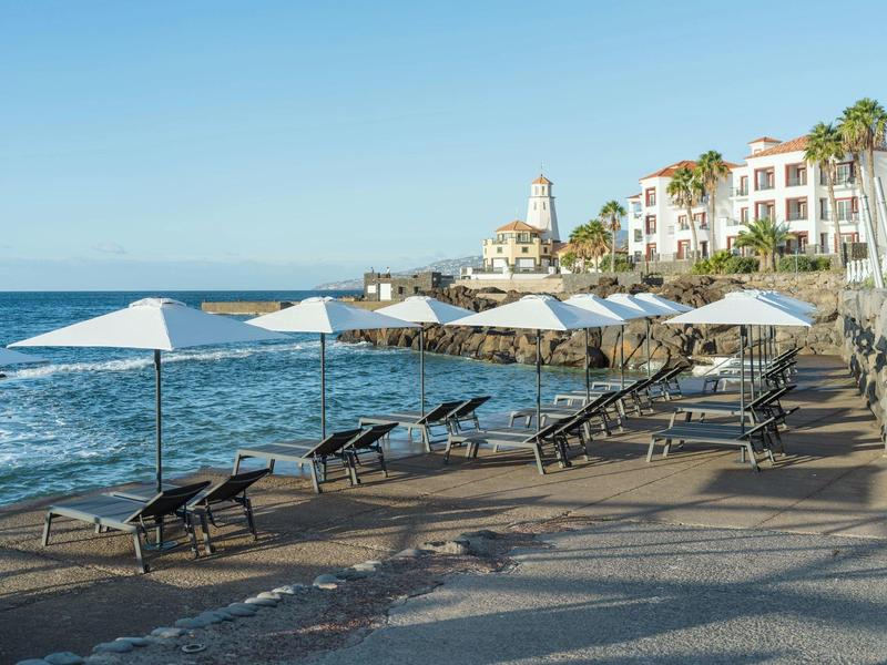 Seaside promenade with sun loungers and umbrellas in front of a hotel.