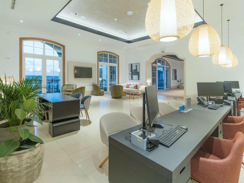 Modern hotel lobby with reception desk, computers, and comfortable seating.