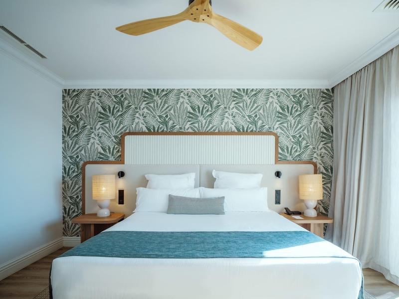 Modern hotel room with large bed, jungle wallpaper, and ceiling fan.