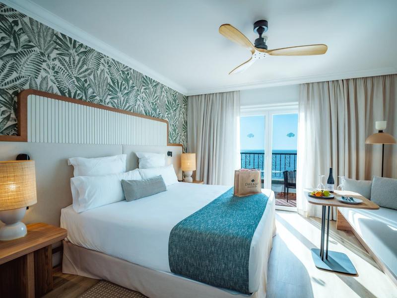 Modern hotel room with large bed, green bedspread, and sea view through window