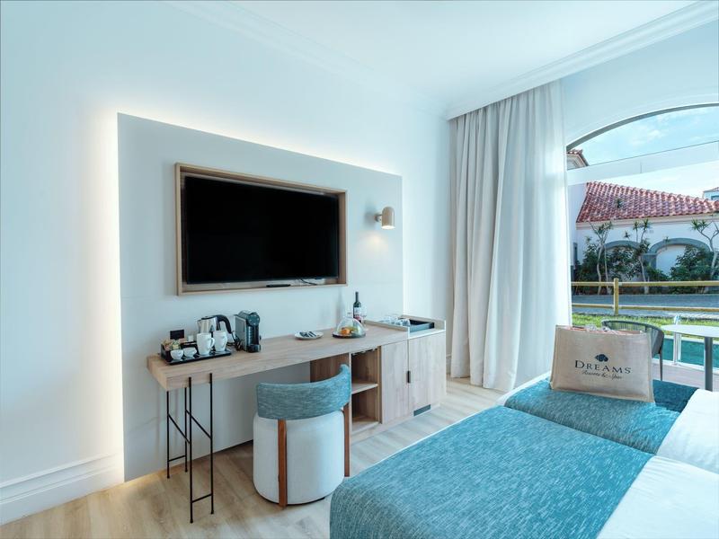 Modern hotel room with TV, desk, chair, and pool view through a sliding glass door.