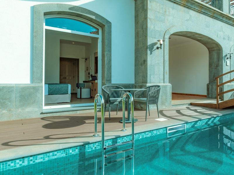 Modern outdoor pool with seating area and access to an indoor space through an open door.