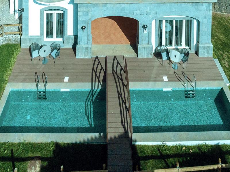 Small pool with bridge in front of a hotel building and seating areas.