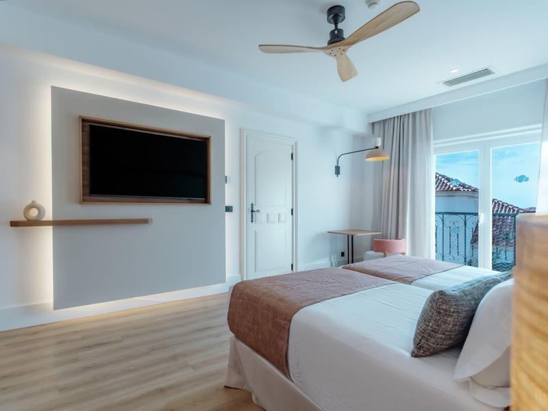 Modern bedroom with double bed, wall TV, and ceiling fan in bright room with balcony.