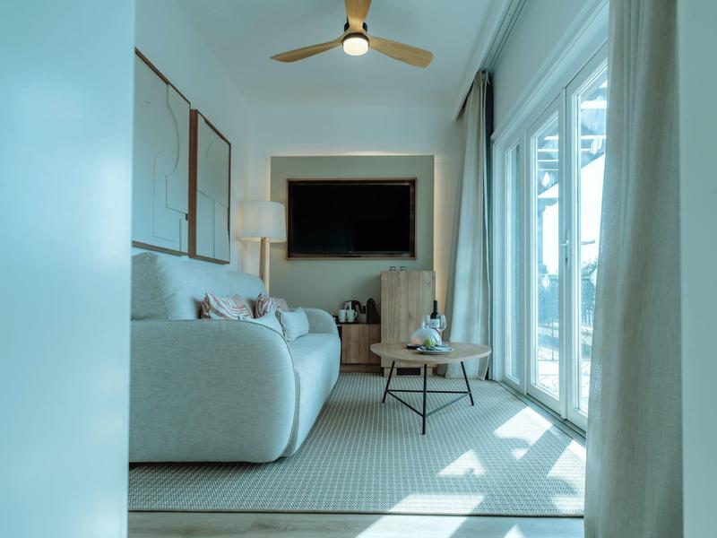 Bright living room with gray sofa, large TV, and floor-to-ceiling windows with curtains.