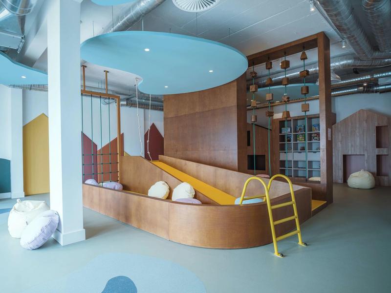 Modern indoor playroom with slide, swings, and climbing elements in a hotel setting.