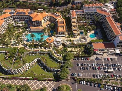 Große Hotelanlage mit roten Dächern, mehreren Pools und großem Parkplatz, umgeben von grüner Natur.