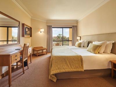 Helles Hotelzimmer mit zwei Betten, Schreibtisch, Stuhl, Spiegel und Balkon mit Blick ins Grüne.