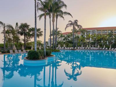 Piscina clara del hotel con palmeras y un atardecer al fondo.