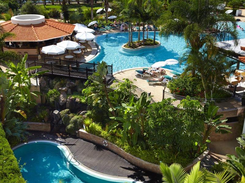 Luxuriöser Hotelpool mit Tropenpflanzen und Meerblick im Hintergrund