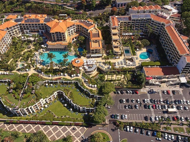 Luftaufnahme eines großen Hotels mit Pool, Gartenanlagen und Parkplätzen am Strand.