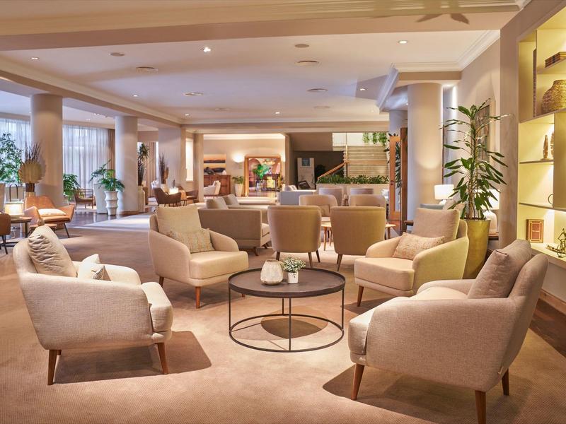 Gemütlicher Hotel-Loungebereich mit Sesseln, runden Tischen und warmem Licht.