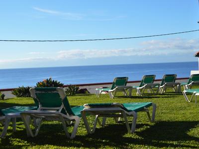 Grüne Liegestühle stehen auf Gras mit Blick auf ruhiges Meer und blauem Himmel.