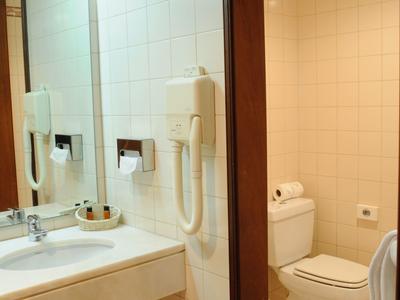 Hell gefliestes Badezimmer mit Waschbecken, Spiegel, Haartrockner und WC in Weiß.