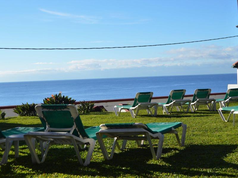 Grüne Liegestühle stehen auf Gras mit Blick auf ruhiges Meer und blauem Himmel.