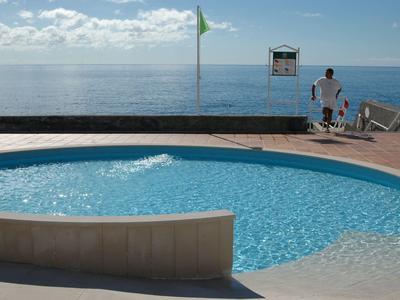 Piscina circolare con acqua blu affacciata sul mare in una giornata di sole.