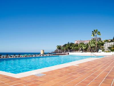 Piscina azzurra limpida con piastrelle terracotta e palme sotto un cielo azzurro.