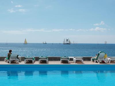 Schwimmbecken mit Liegestühlen am Meer und Segelbooten auf dem Wasser