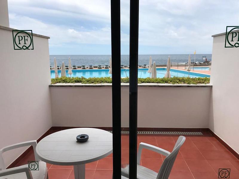 Vista da un balcone con due sedie e un tavolo verso il mare e la piscina.