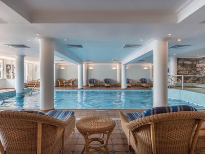 Piscina coperta con sedie in vimini e tavoli rotondi in una spa dell'hotel con illuminazione soffusa.