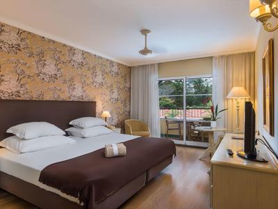 Camera d'hotel accogliente con letto matrimoniale, carta da parati floreale e balcone con vista sul verde.