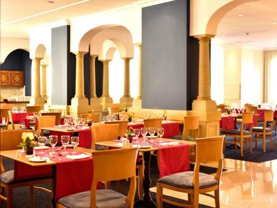 Zona ristorante luminosa con tovaglie rosse e sedie in legno.