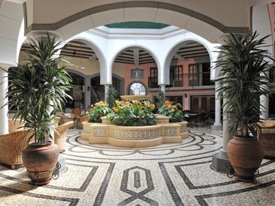 Cortile luminoso con fontana, grandi piante e galleria circostante in tonalità calde.
