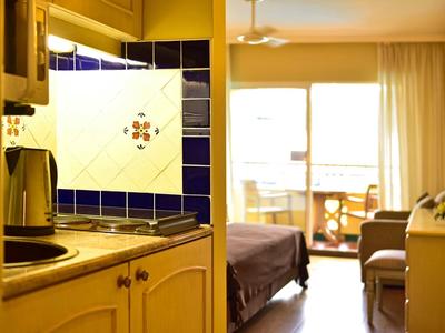 Camera d'hotel luminosa con letto, balcone e angolo cottura con piastrelle blu.