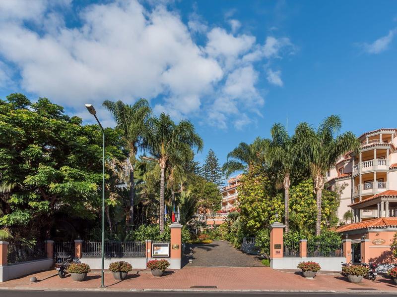 Ingresso dell'hotel con palme e muri di mattoni rossi sotto un cielo azzurro.
