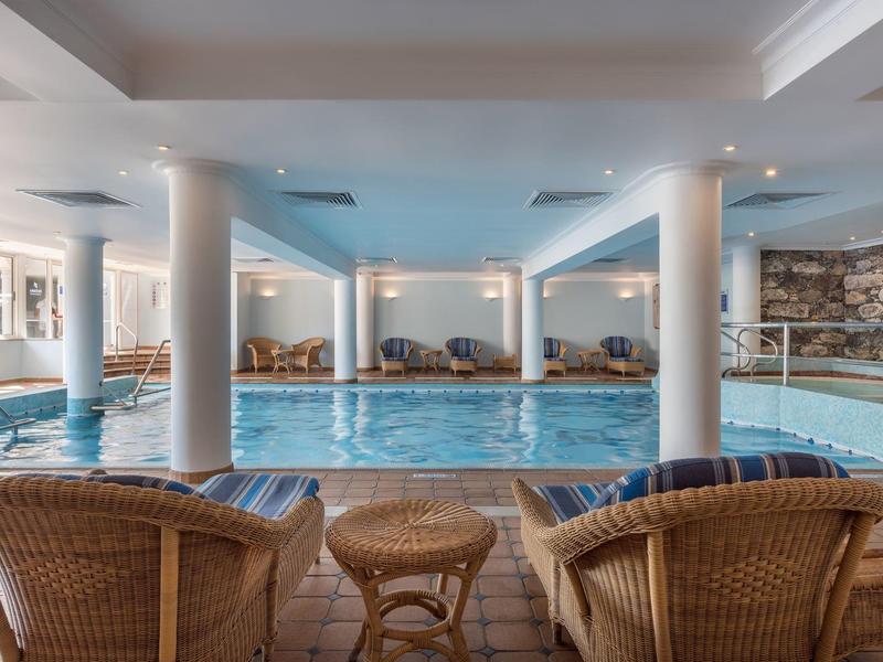 Piscina coperta con sedie in vimini e tavoli rotondi in una spa dell'hotel con illuminazione soffusa.