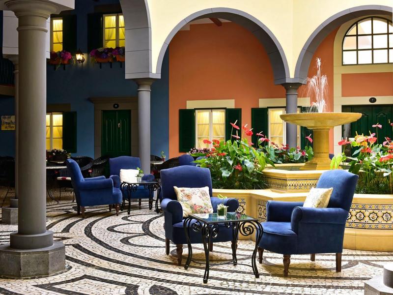 Cortile con poltrone blu e fontana, circondato da finestre e porte ad arco.