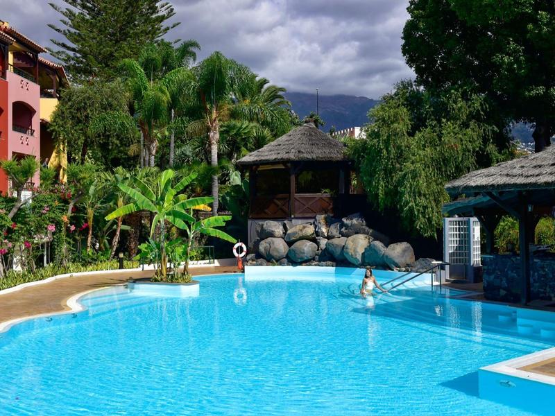 Grande piscina con acqua limpida circondata da palme, edifici colorati e capanne.