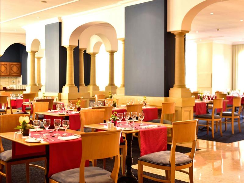 Zona ristorante luminosa con tovaglie rosse e sedie in legno.