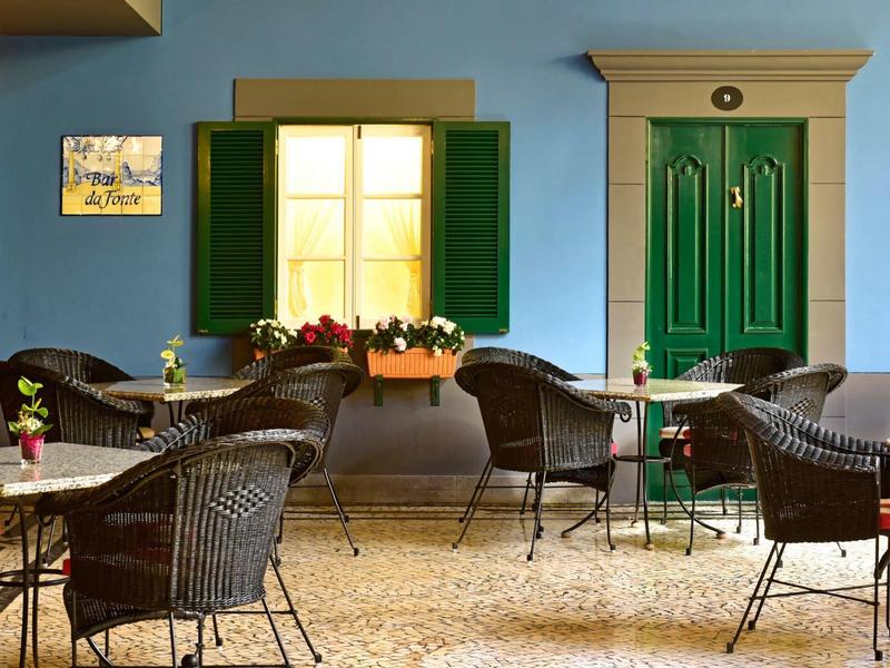 Accogliente area esterna di un caffè con sedie in vimini scuro e tavoli davanti a un edificio blu.