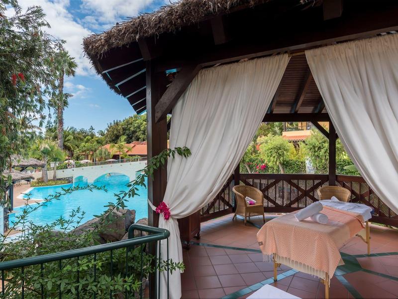 Area massaggi coperta con vista su una piscina e piante tropicali.